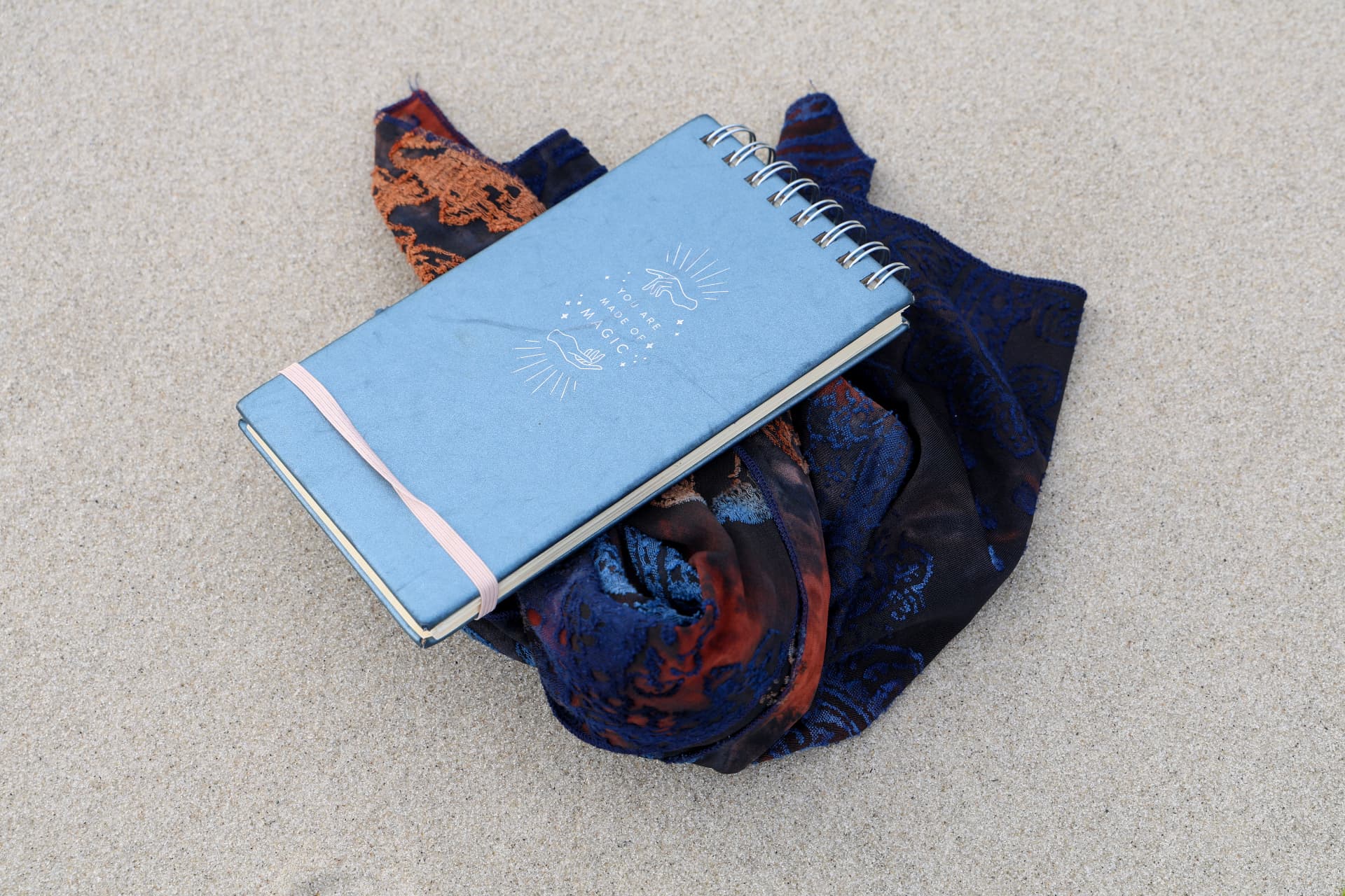 A blue journal resting on a patterned scarf in the sand