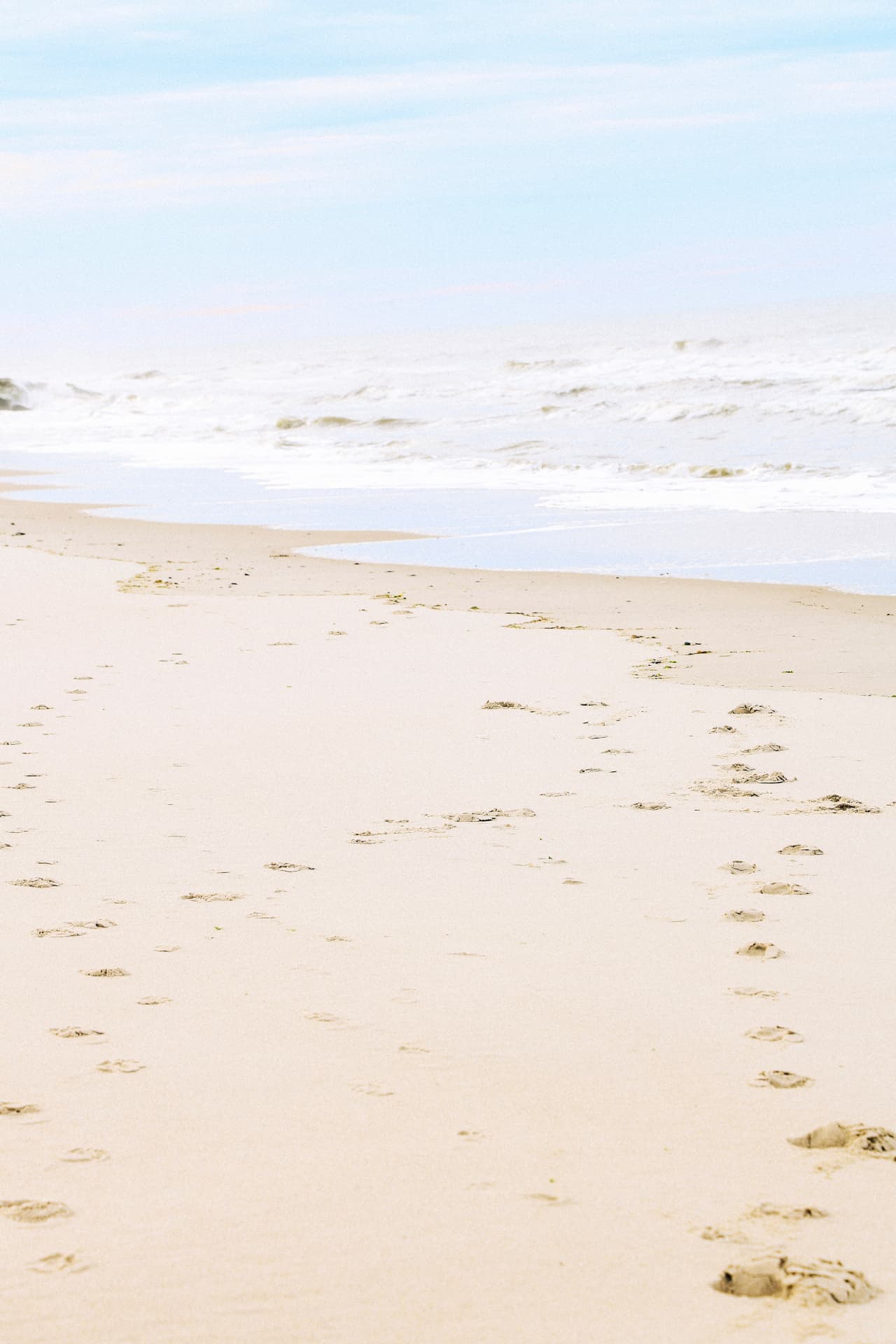 Ocean foam moving diagonally across warm sand with footprints